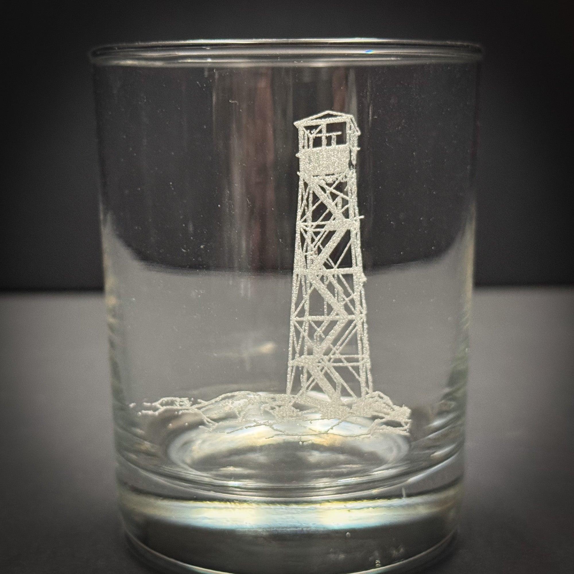 A clear glass with a white lighthouse etched into it.