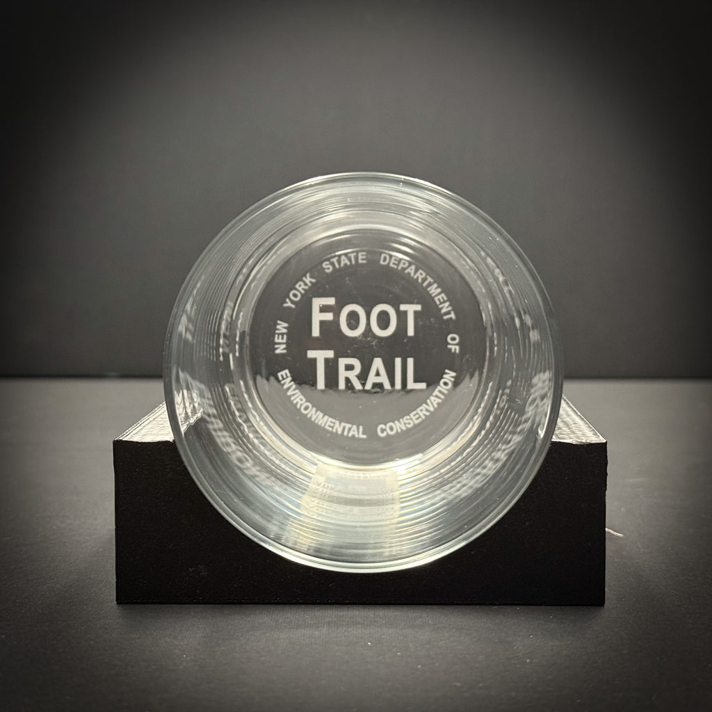 A clear glass with the text "FOOT TRAIL ENVIRONMENTAL CONSERVATION" printed on it, placed on a black surface.