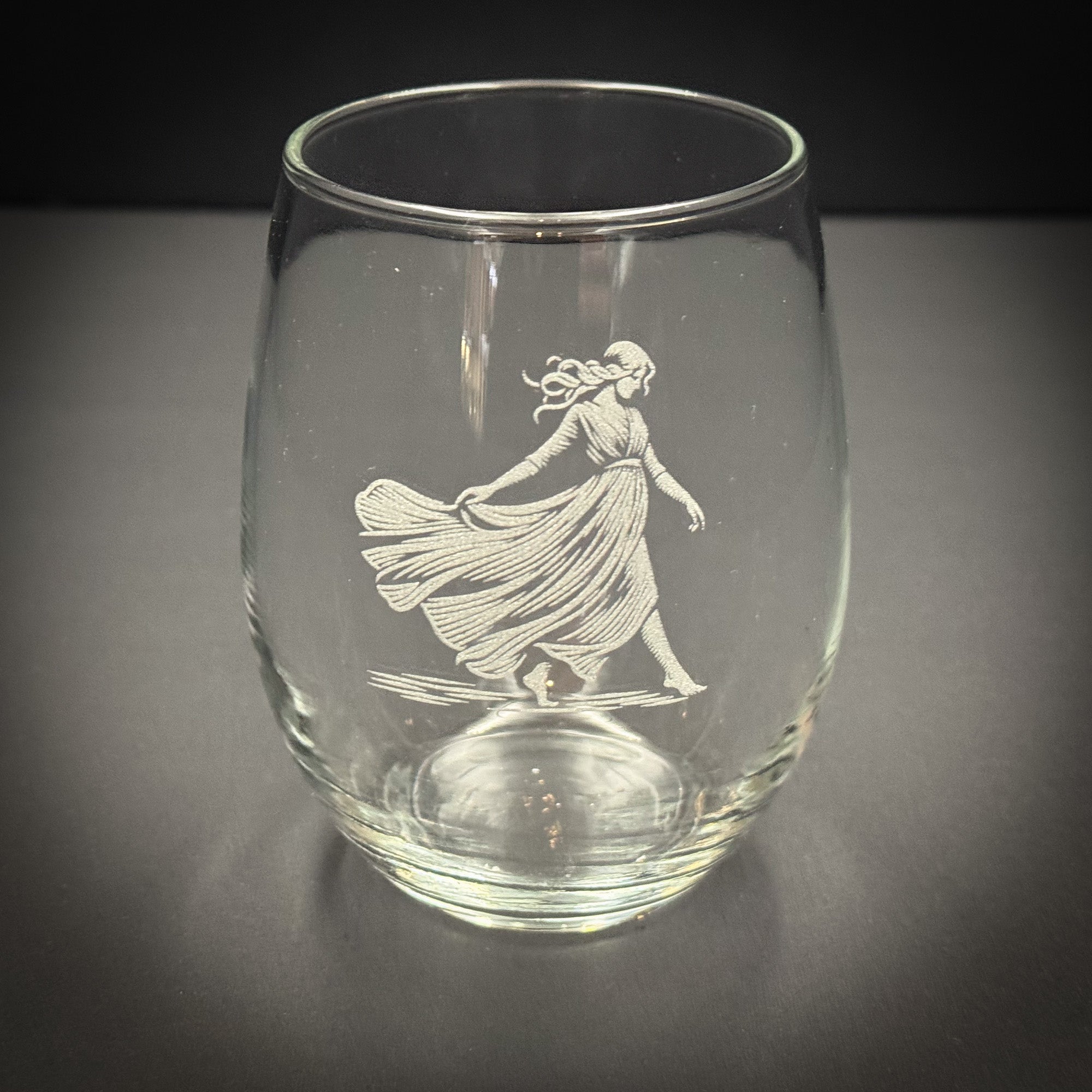 A glass with an etched image of a woman in a flowing dress on it.