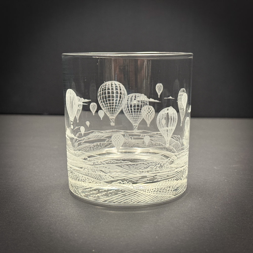 A clear glass with an etched design of hot air balloons floating in the sky.