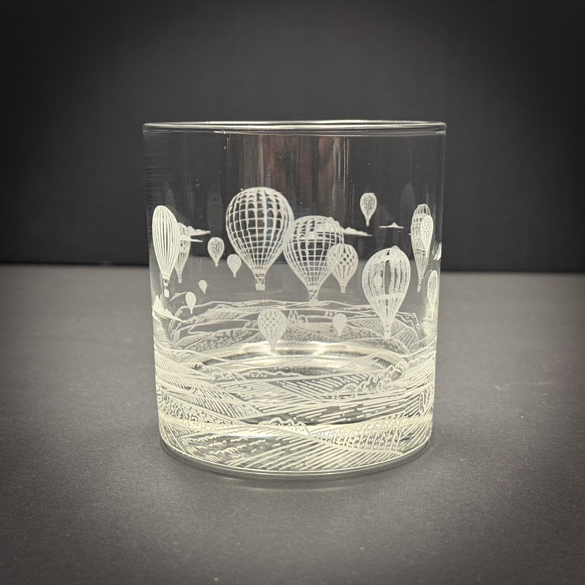 A clear glass with an etched design of hot air balloons floating in the sky.
