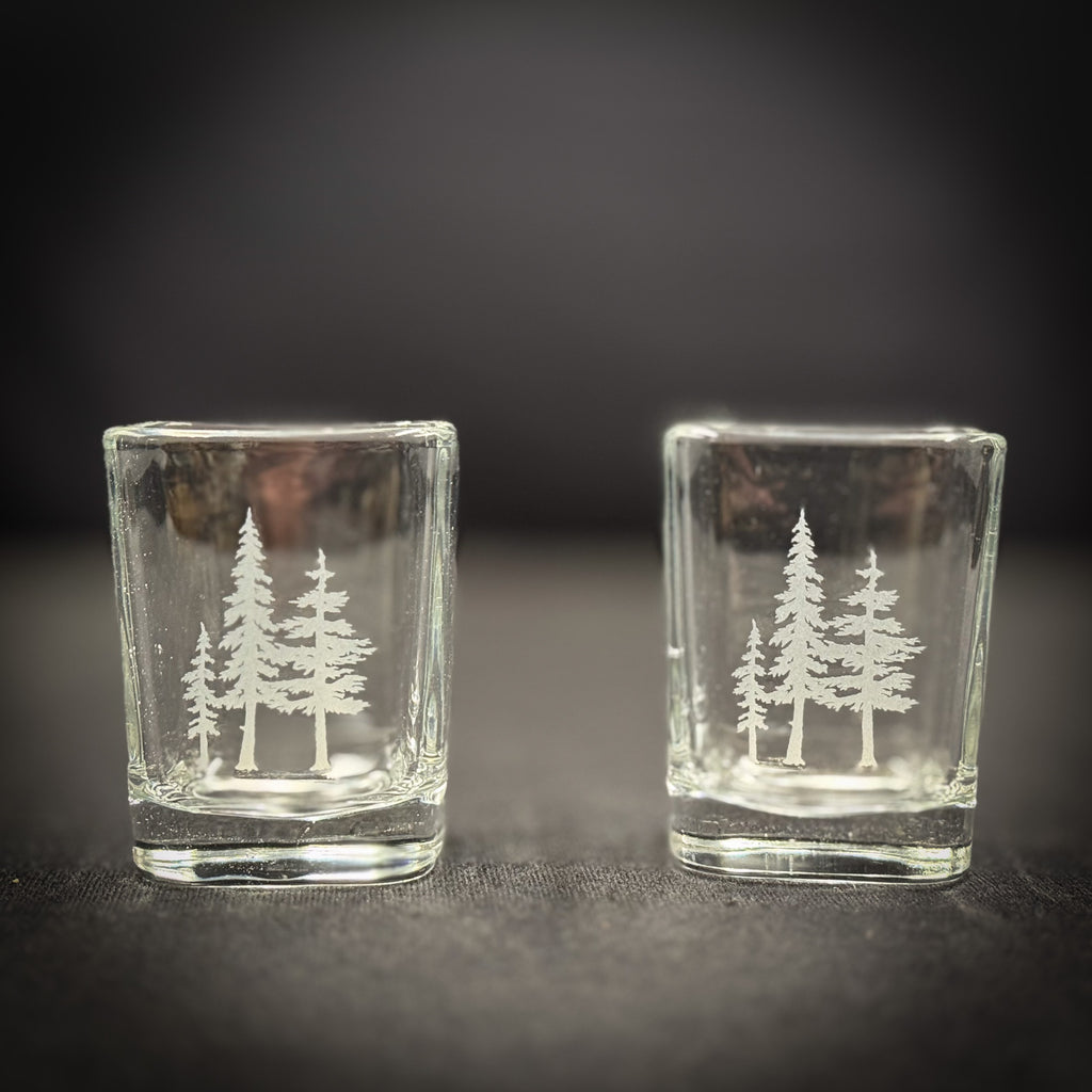 Two clear glass tumblers with white tree silhouettes printed on them, placed side by side on a dark surface.