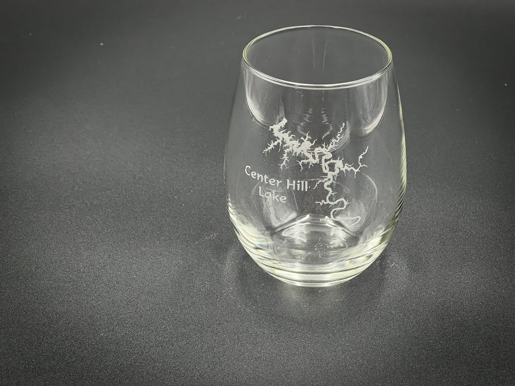 A clear glass with a design etched into it, sitting on a dark surface.