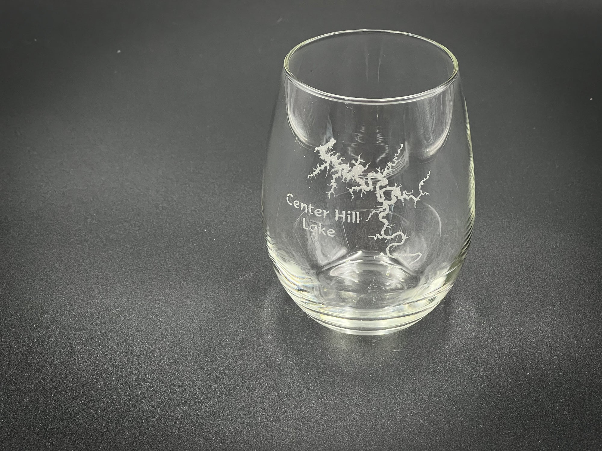 A clear glass with a design etched into it, sitting on a dark surface.