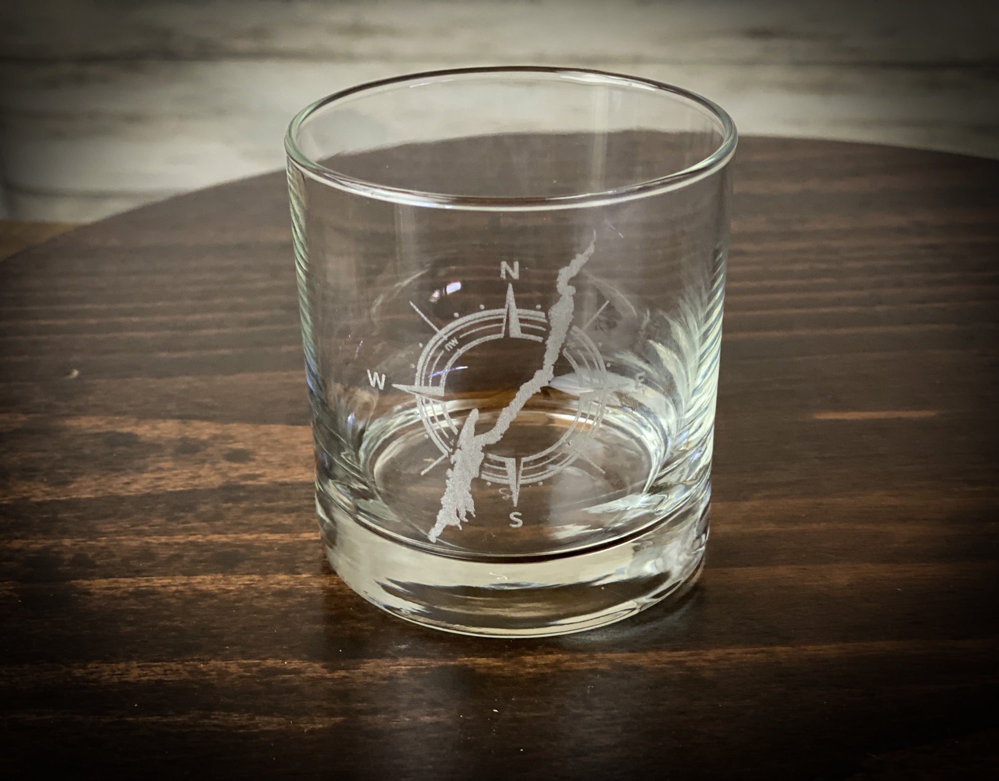 A clear glass with a compass design etched onto it, sitting on a wooden surface.