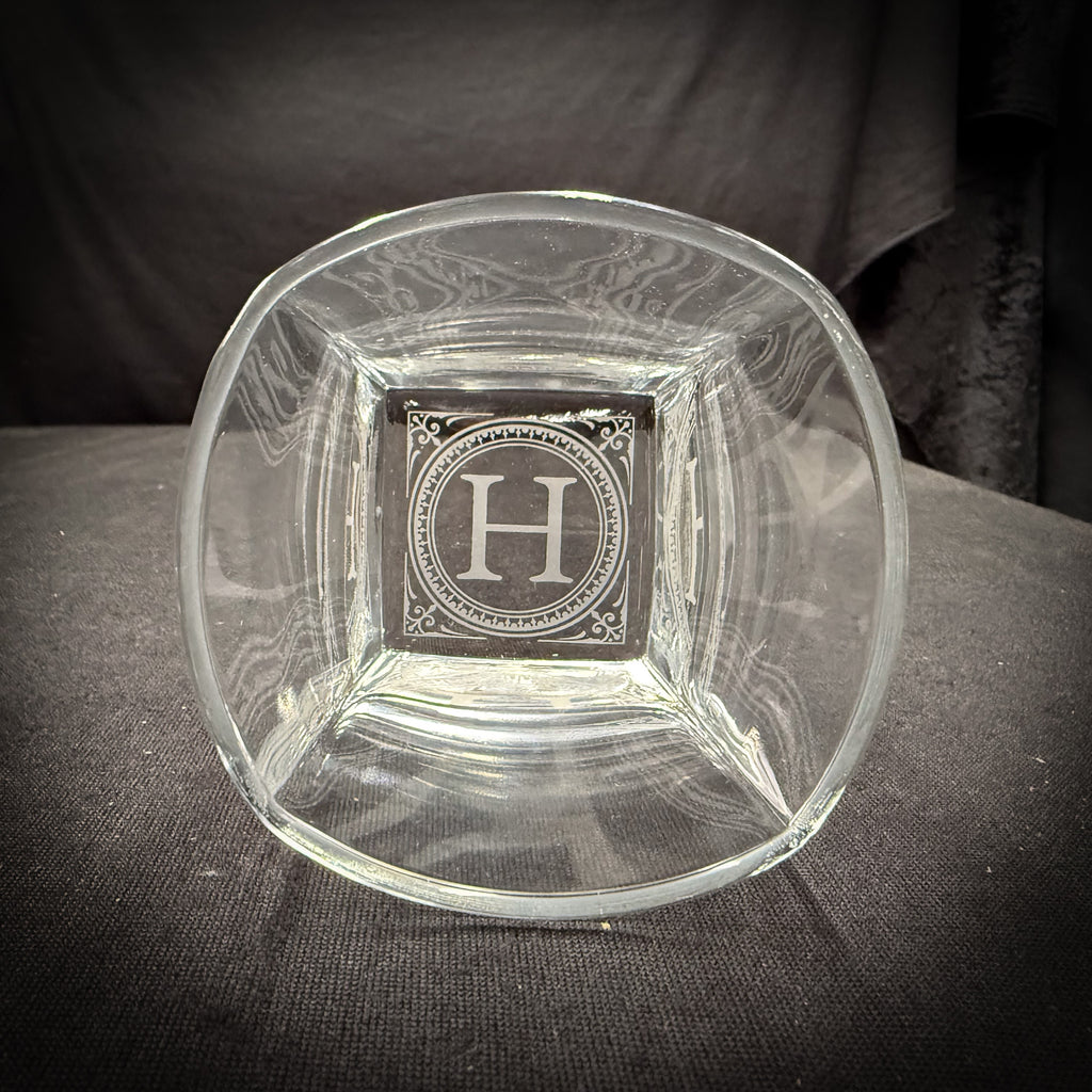 A clear glass bowl with an engraved letter "H" in the center.