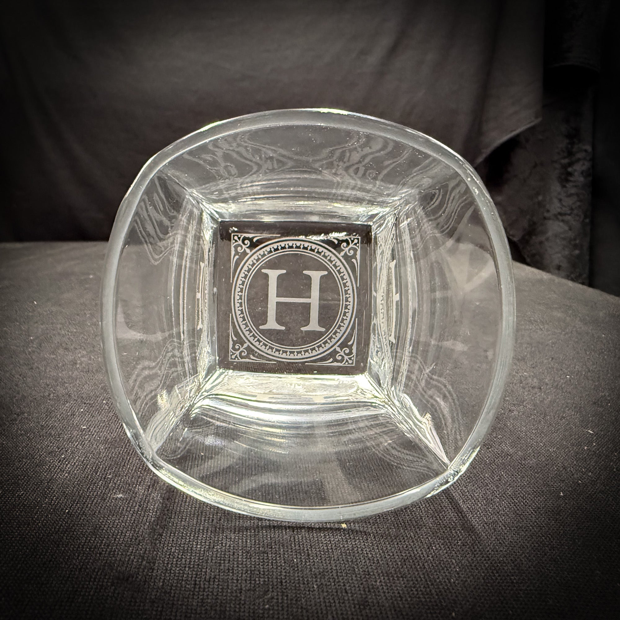 A clear glass bowl with an engraved letter "H" in the center.
