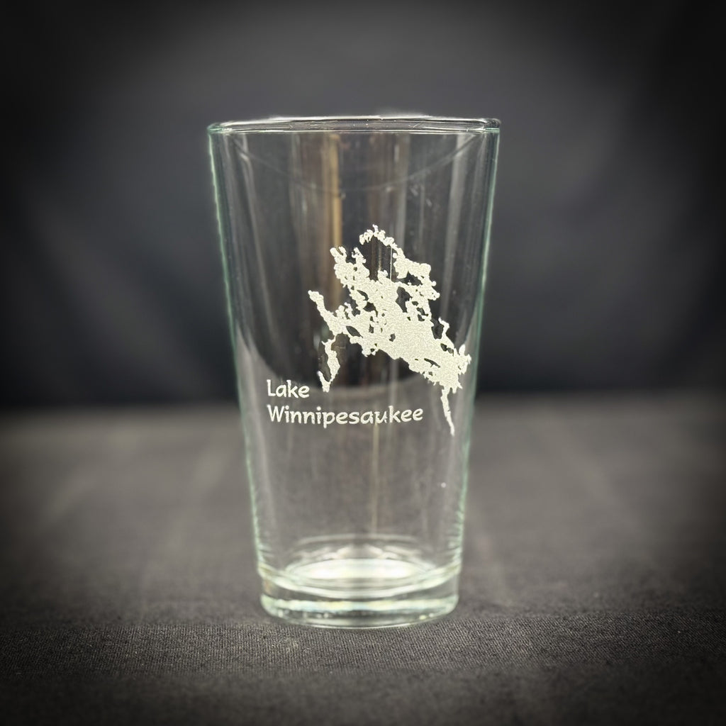 A clear glass with a white design on it, featuring a map of Lake Winnipesaukee.