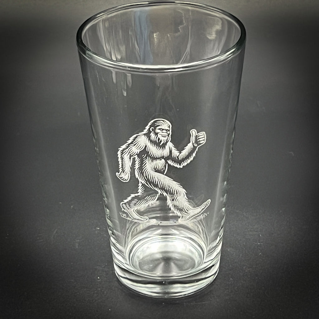 A clear glass with an etched image of a Sasquatch, a mythical creature, on it.
