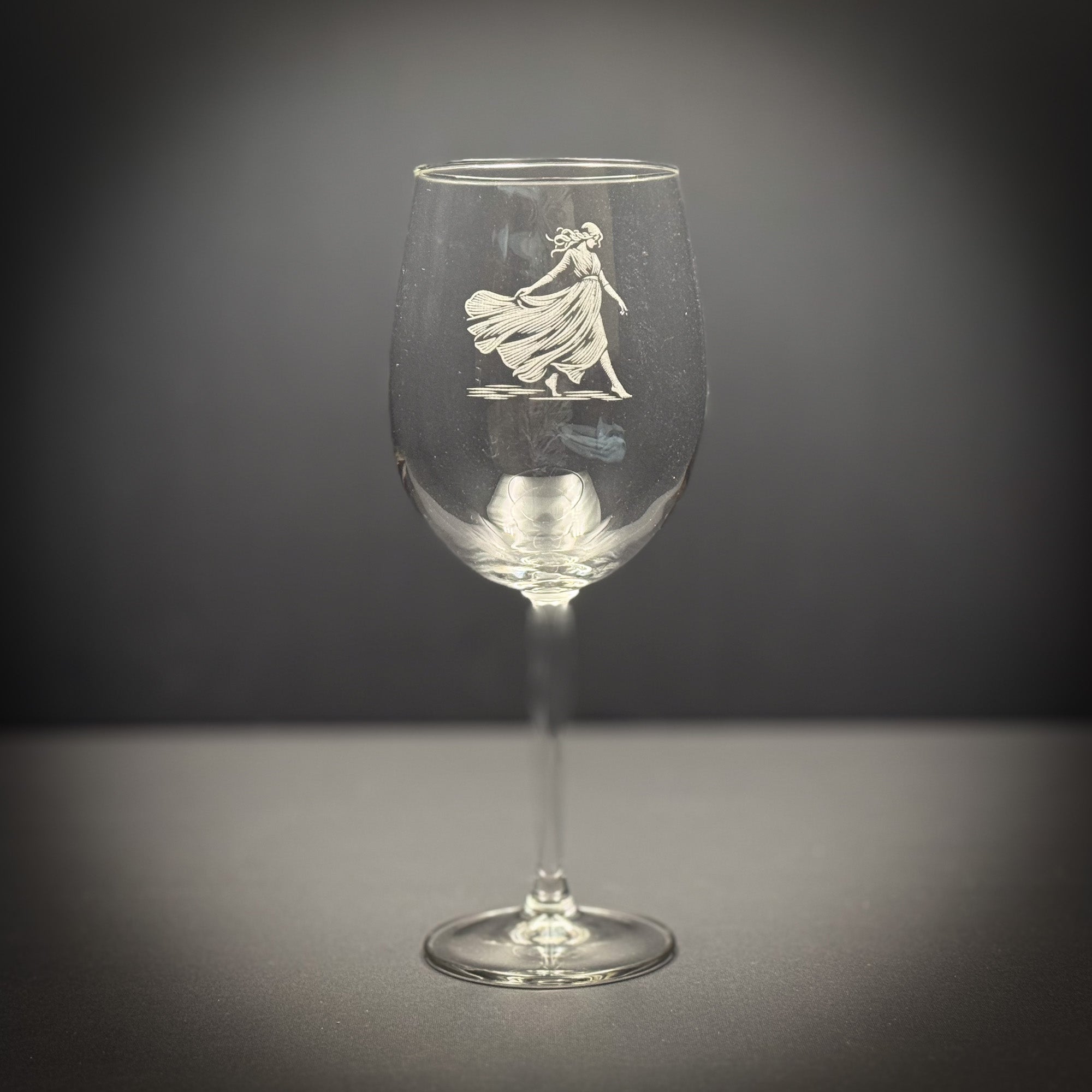 A wine glass with an etched image of a woman in a flowing dress on the stem.
