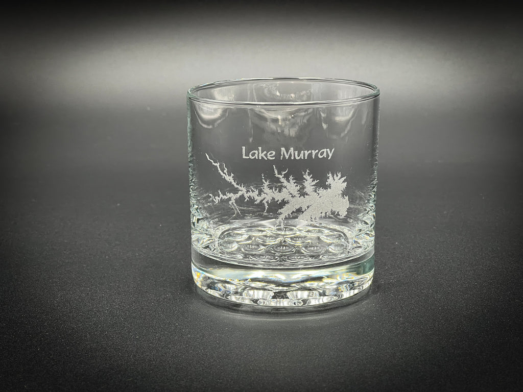 A clear glass with a design etched into it, featuring a stylized tree or plant pattern.