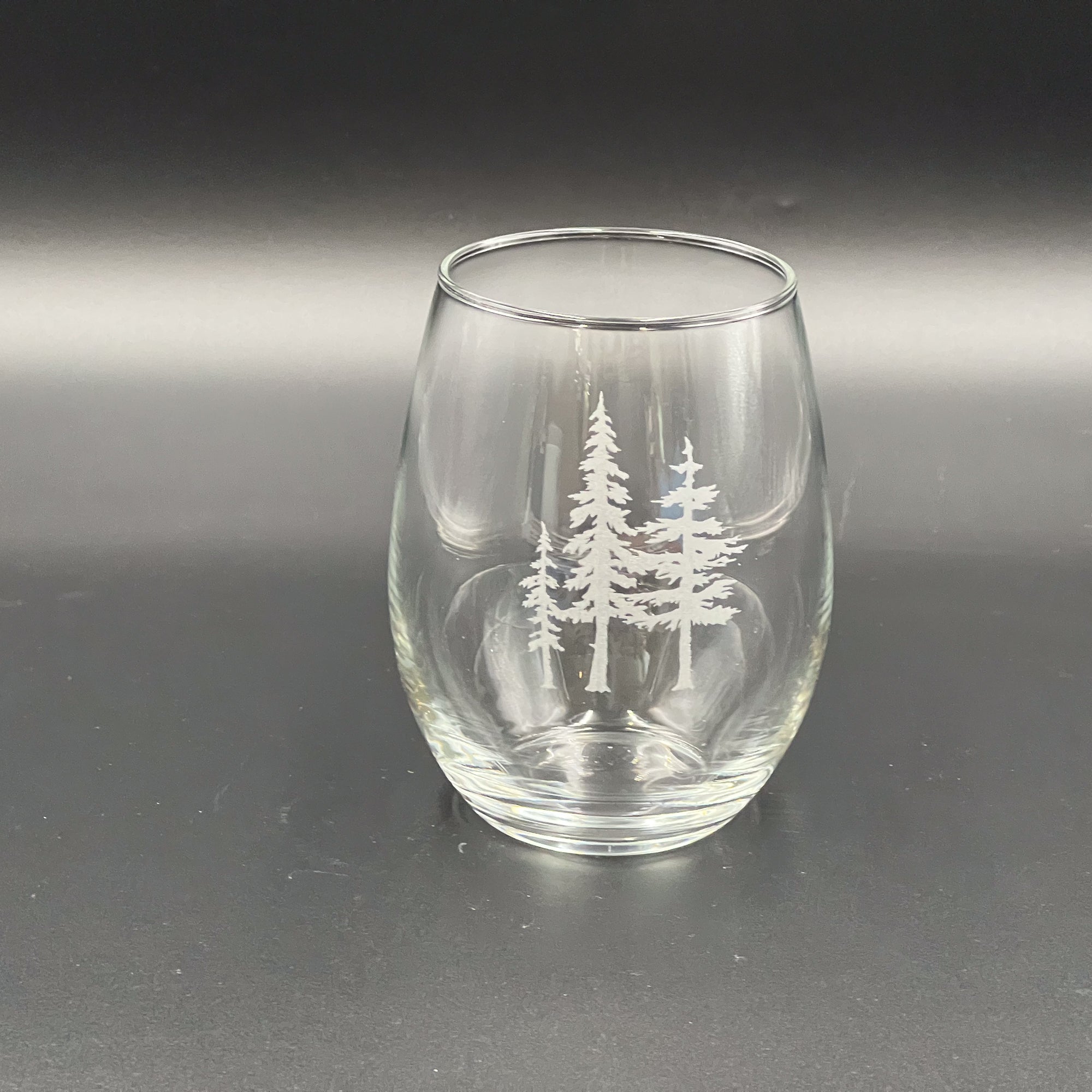A clear glass with a white tree design etched on it, sitting on a dark surface.