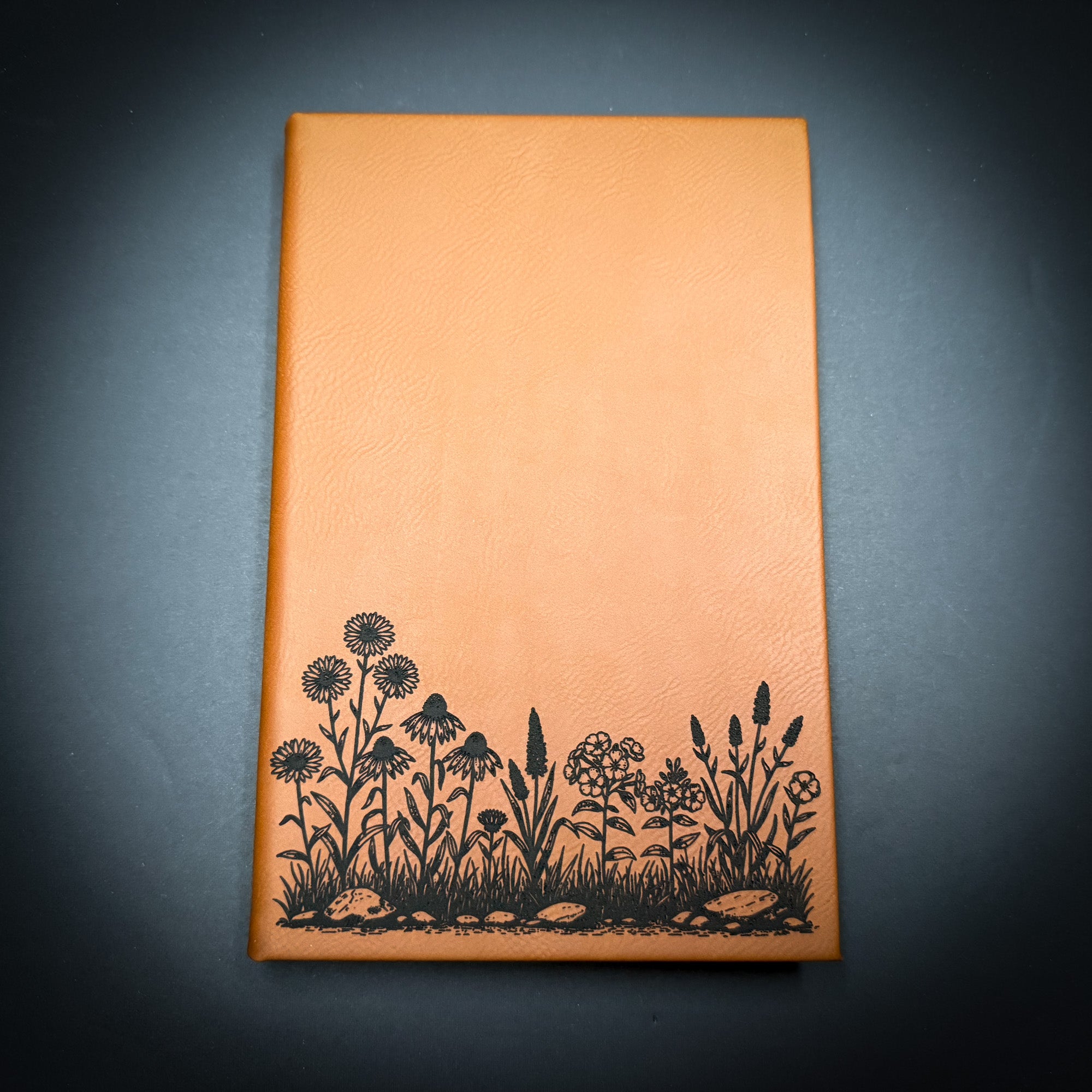 a rectangular, orange-colored notebook with a black floral design on the cover.