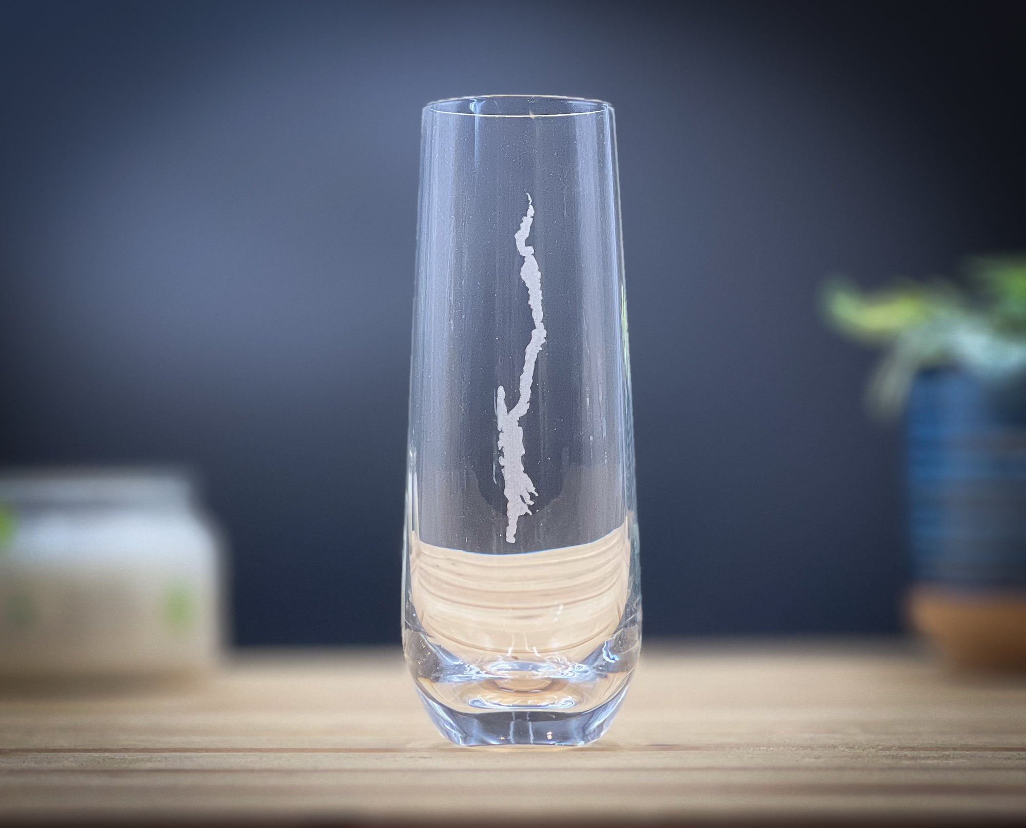 A clear glass vase with a white design etched into it, placed on a wooden surface.
