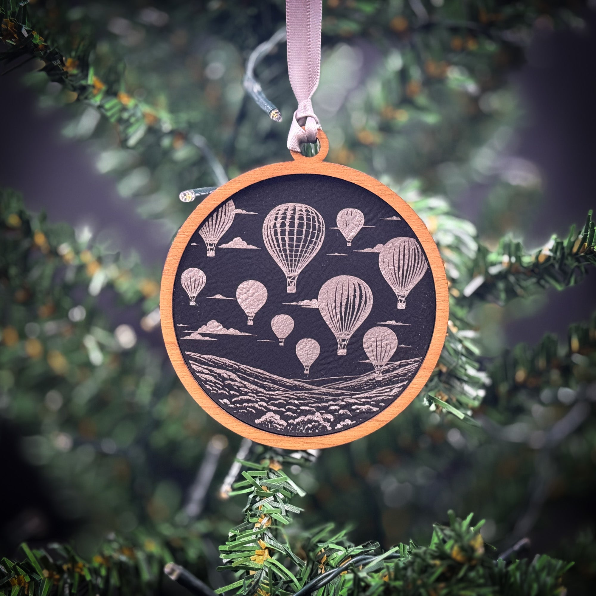 A circular ornament hanging from a tree, featuring a black background with white hot air balloons floating in the sky.