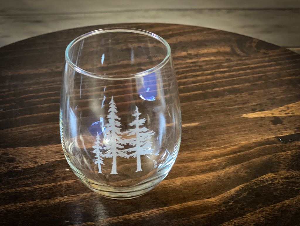 A clear glass with a white tree design on it, placed on a wooden surface.