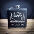 A black leather flask with a silver cap and a white illustration of a moose in a forest setting.