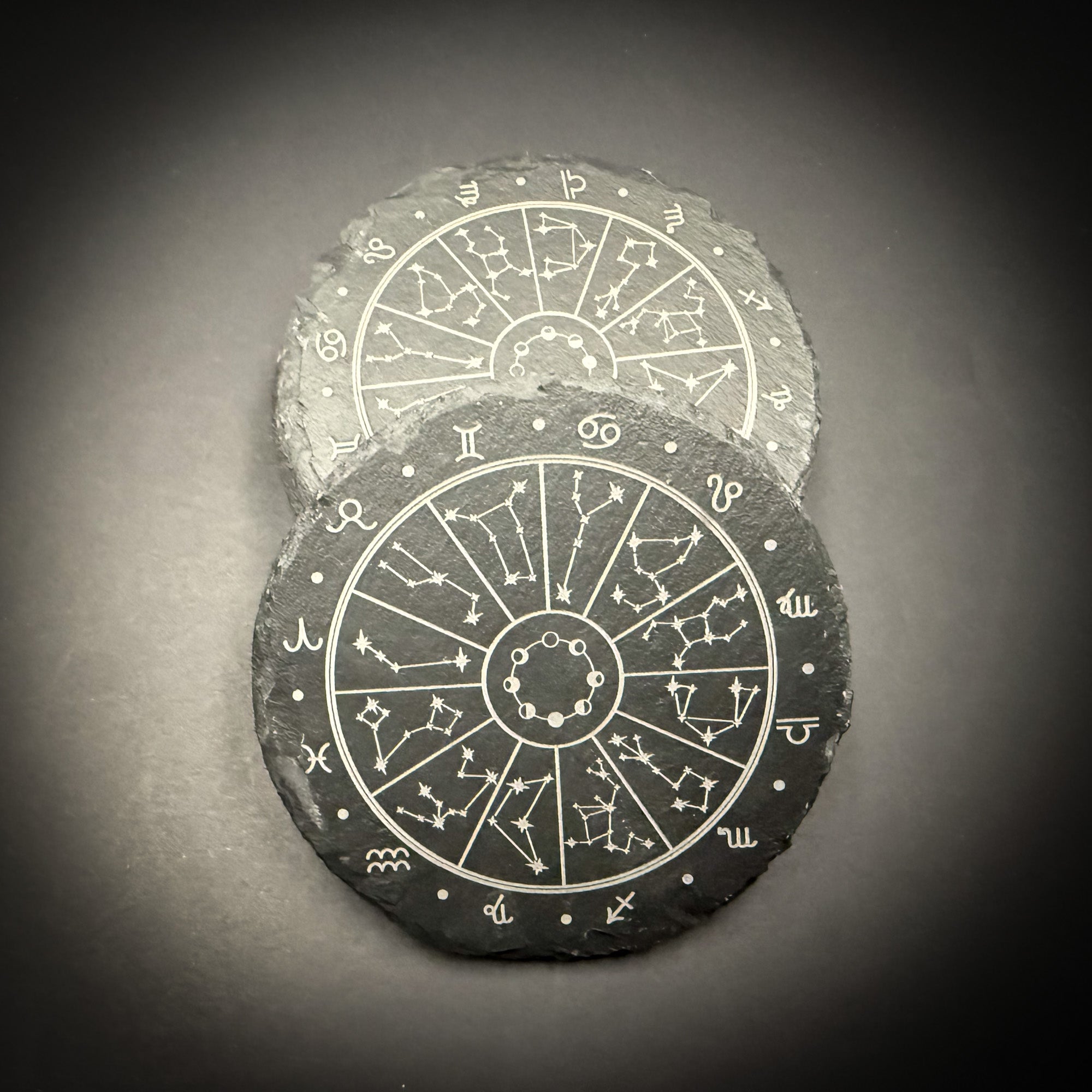 two circular coasters with astrological symbols and zodiac signs printed on them.