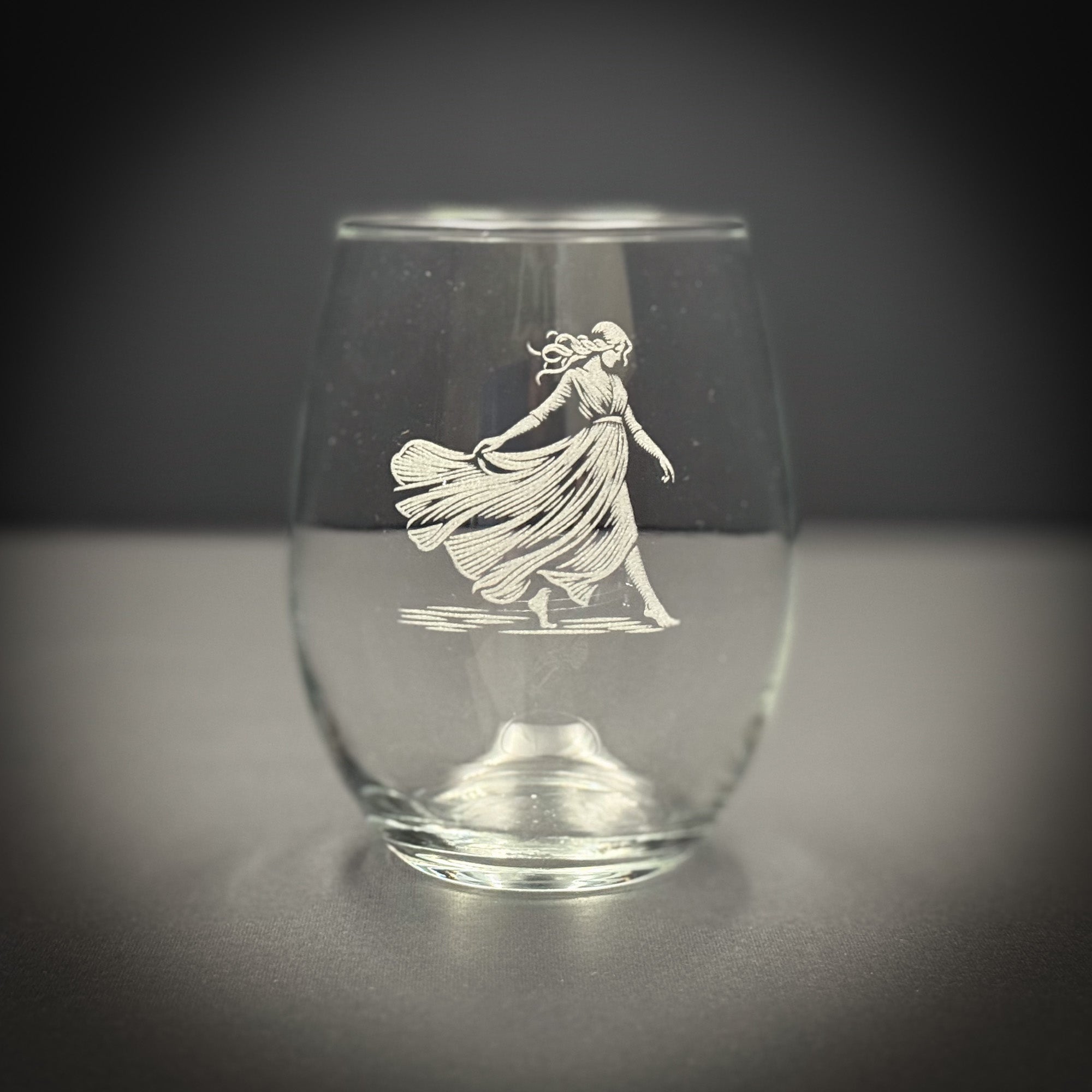 A glass with an etched image of a woman in a flowing dress on it.