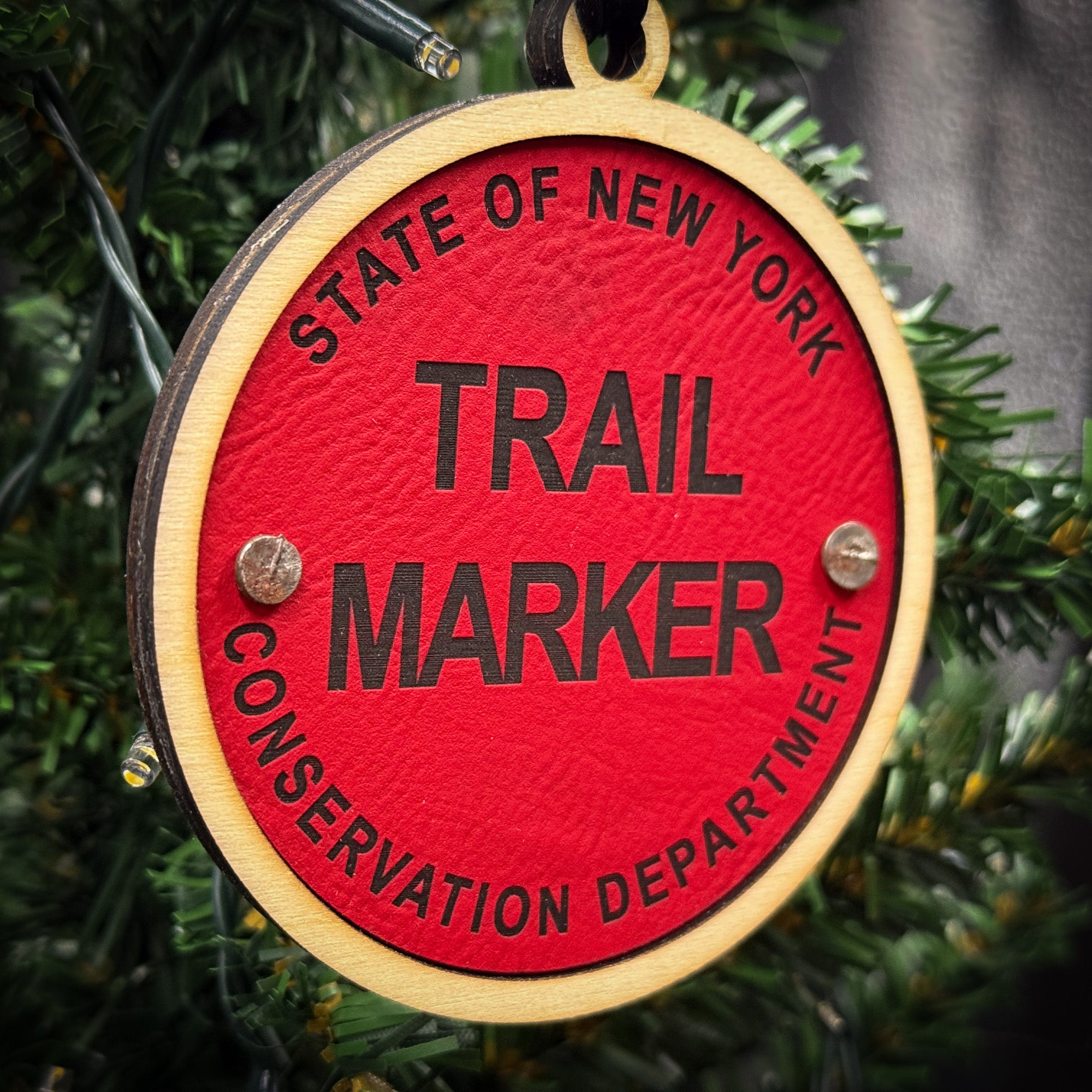 A red ornament with the words "Trail Marker" and "Conservation Department" printed on it, hanging on a Christmas tree.