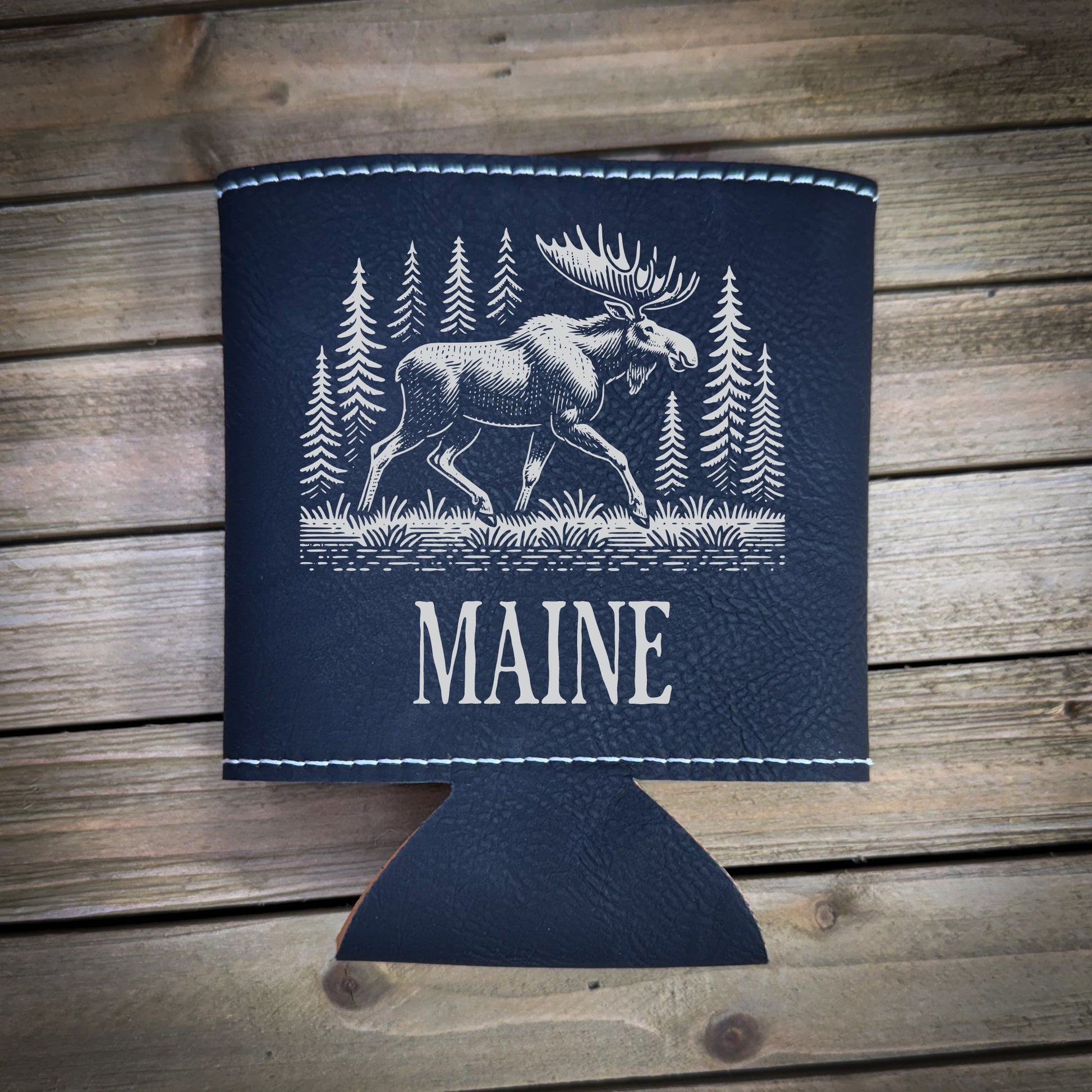 A black leather cooler with a white moose illustration and the word "MAINE" printed on it, placed on a wooden surface.
