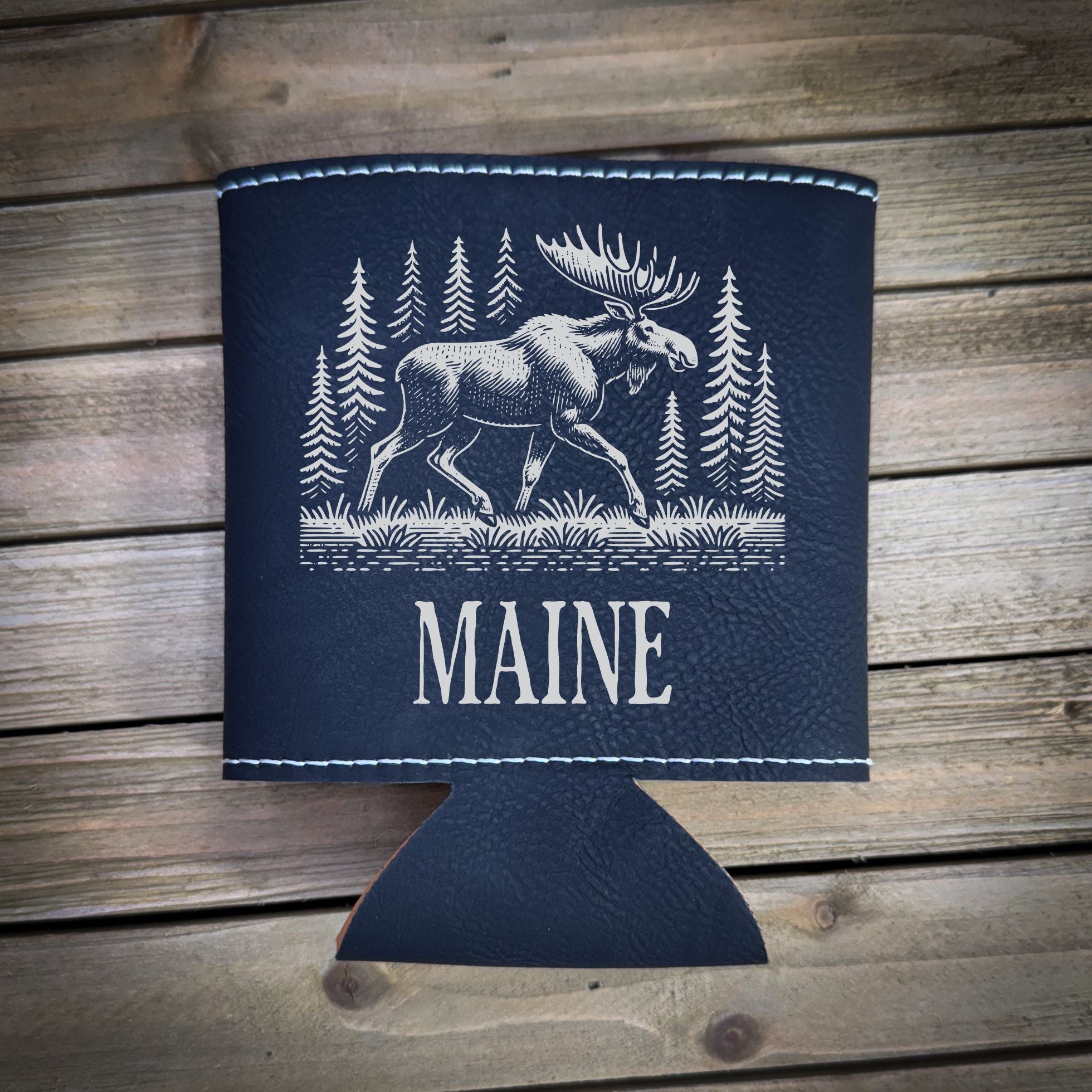 A black leather cooler with a white moose illustration and the word "MAINE" printed on it, placed on a wooden surface.