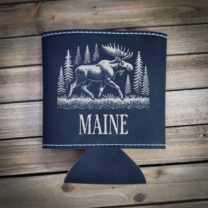 A black leather cooler with a white moose illustration and the word "MAINE" printed on it, placed on a wooden surface.