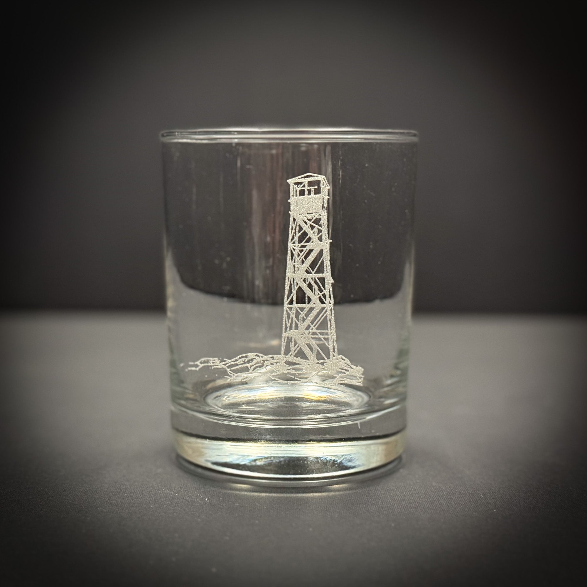 A clear glass with an etched image of a lighthouse on it.