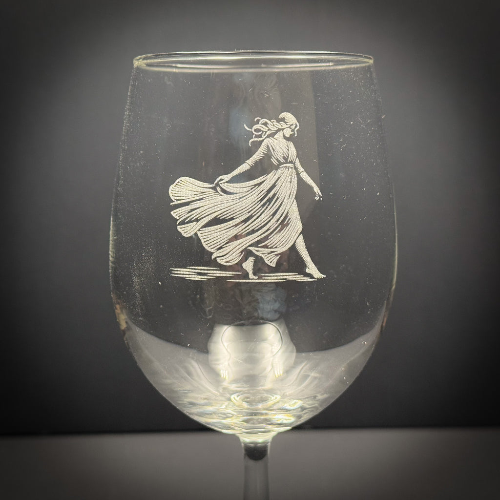 a wine glass with an etched image of a woman in a flowing dress.