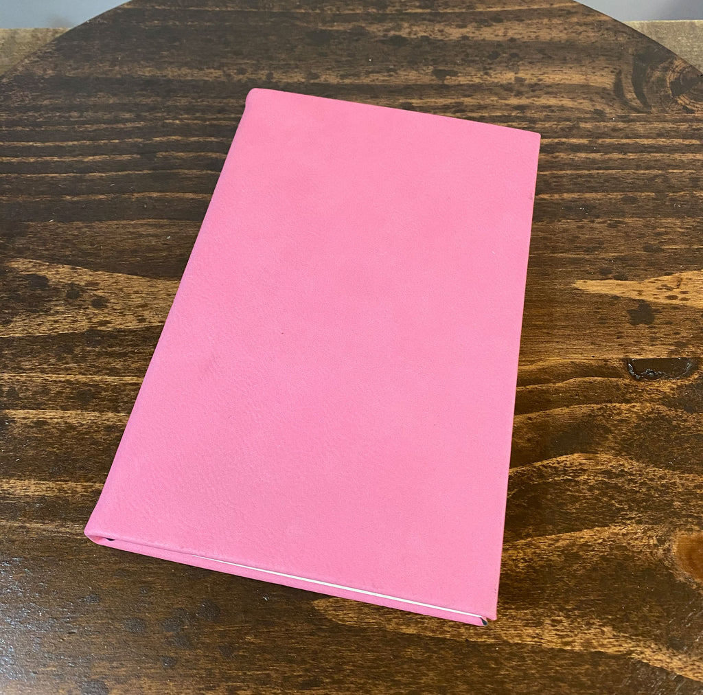 A pink notebook is lying on a wooden surface.