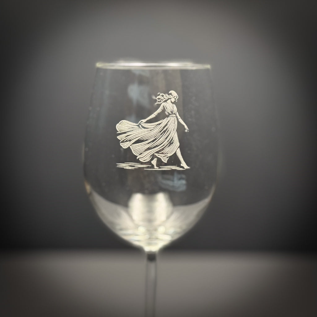 A wine glass with an etched image of a woman in a flowing dress on it.