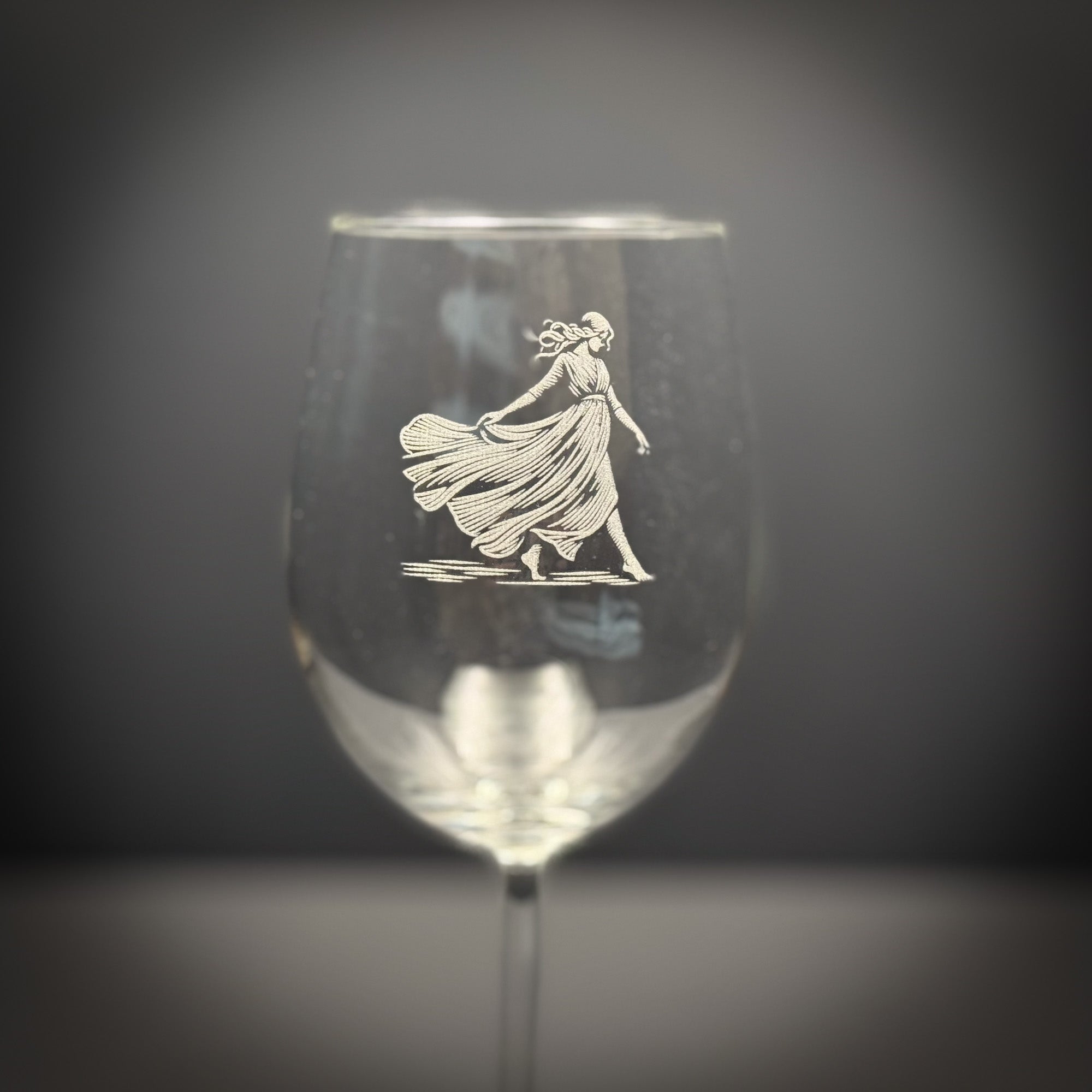 A wine glass with an etched image of a woman in a flowing dress on it.