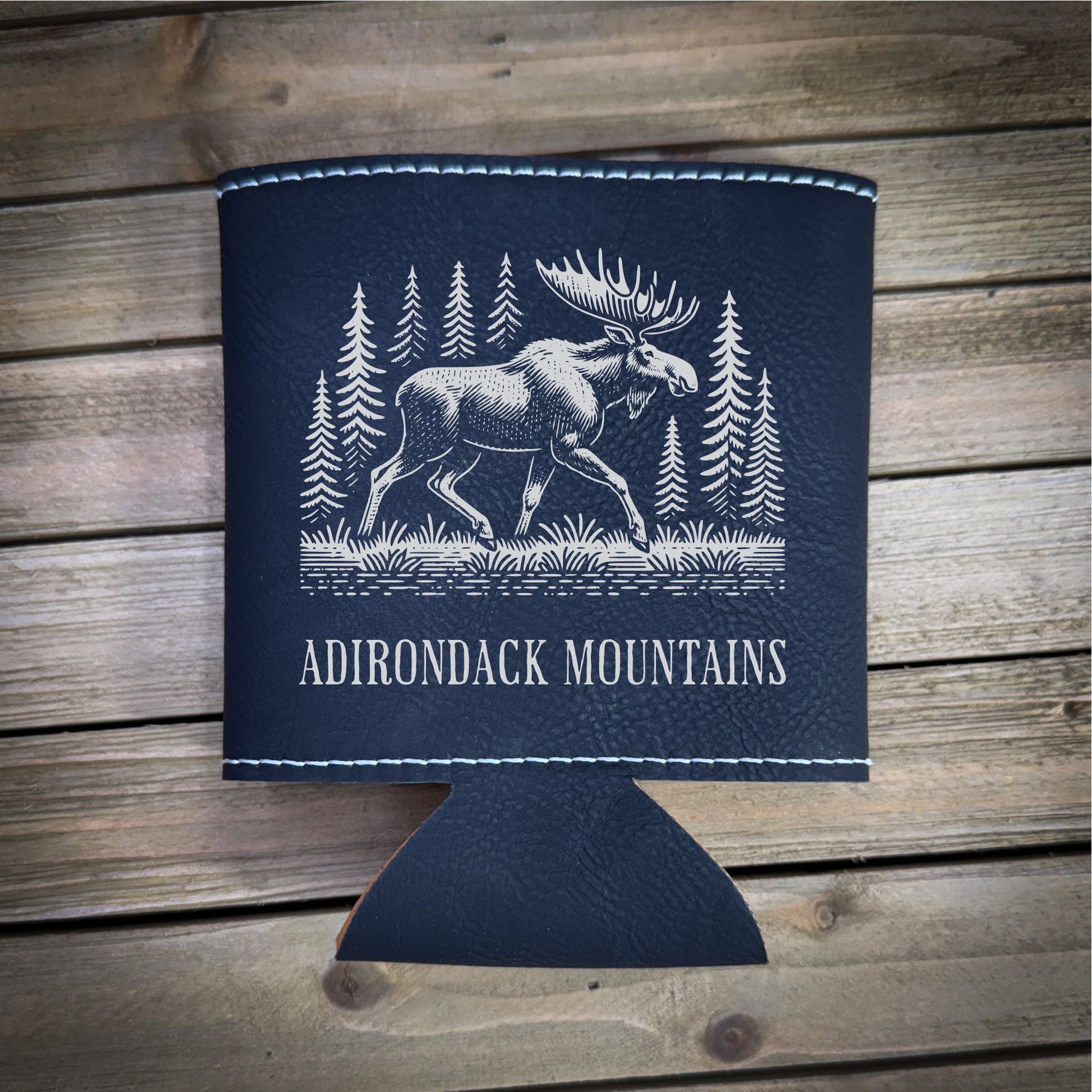 A black leather cooler with a white illustration of a moose and pine trees, along with the text "ADIRONDACK MOUNTAINS" printed on it.