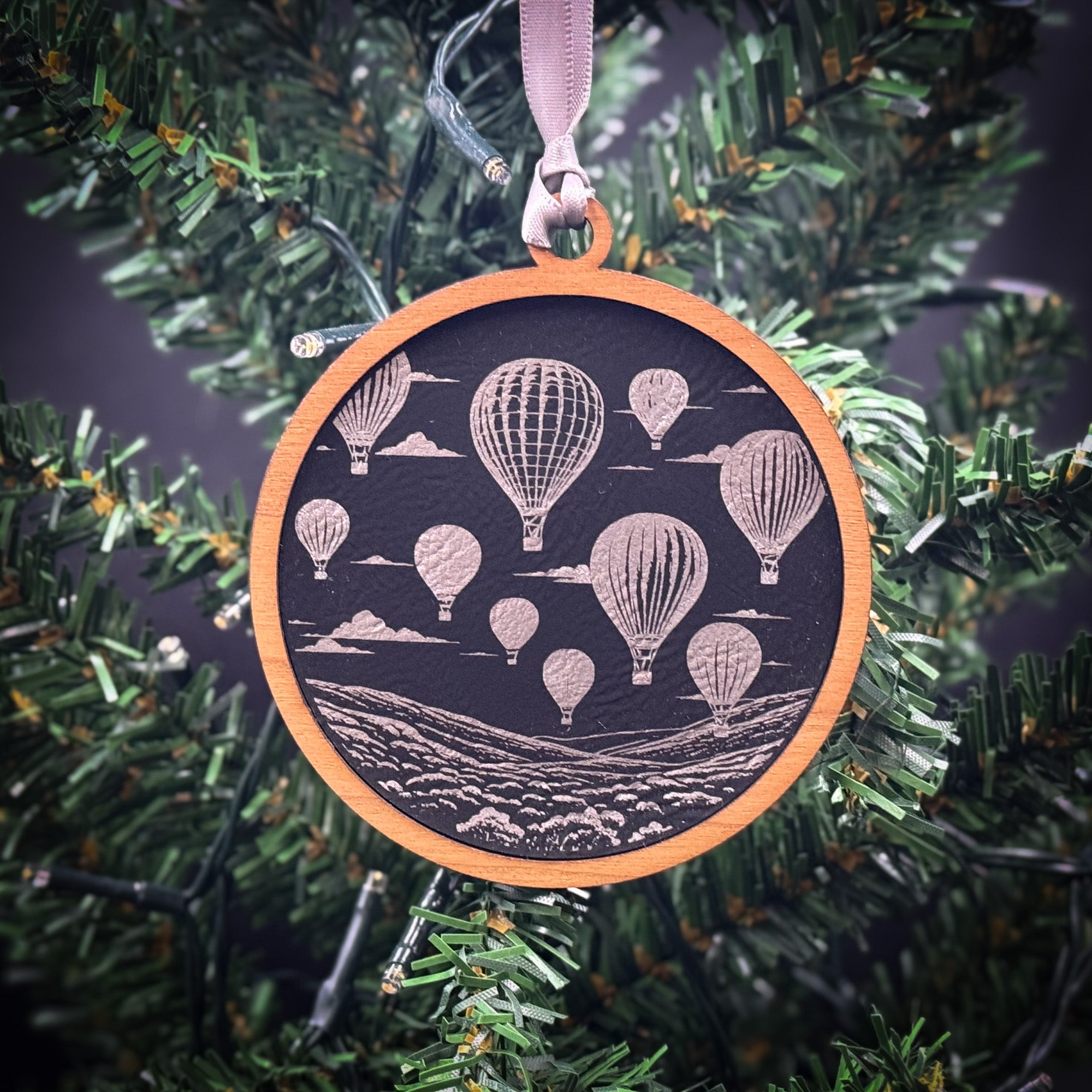 A circular ornament hanging from a Christmas tree, featuring a black background with illustrations of hot air balloons floating in the sky.