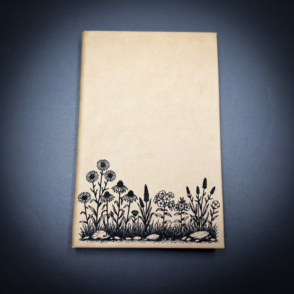 A beige-colored notebook with a black and white illustration of flowers and plants printed on the cover.