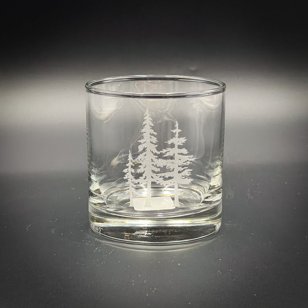 A clear glass with a white tree design etched onto it, sitting on a dark surface.
