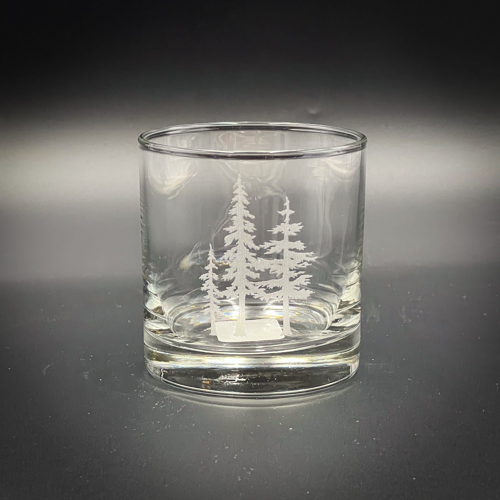A clear glass with a white tree design etched onto it, sitting on a dark surface.