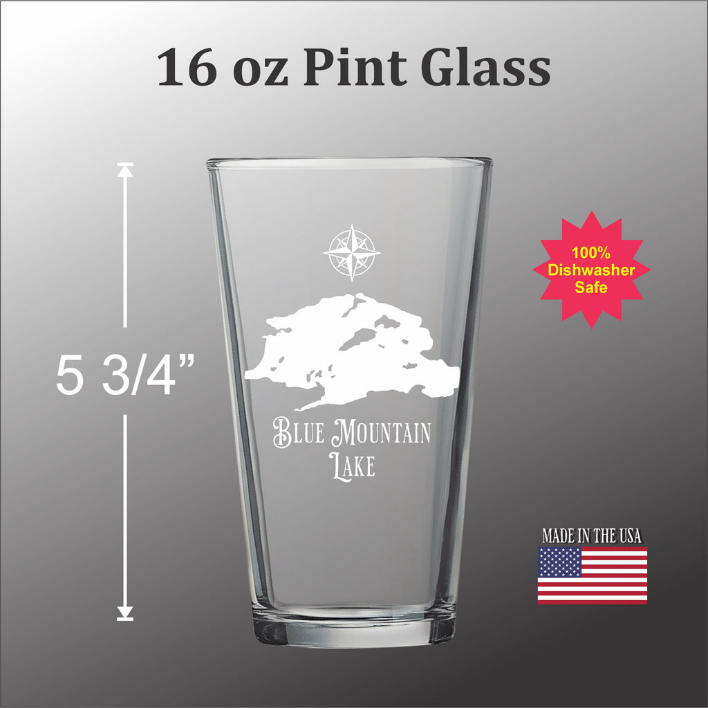 A pint glass with a design of a mountain and lake on it, along with some text and measurements.