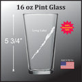 a pint glass with a design of a lake on it, along with some text and a logo.