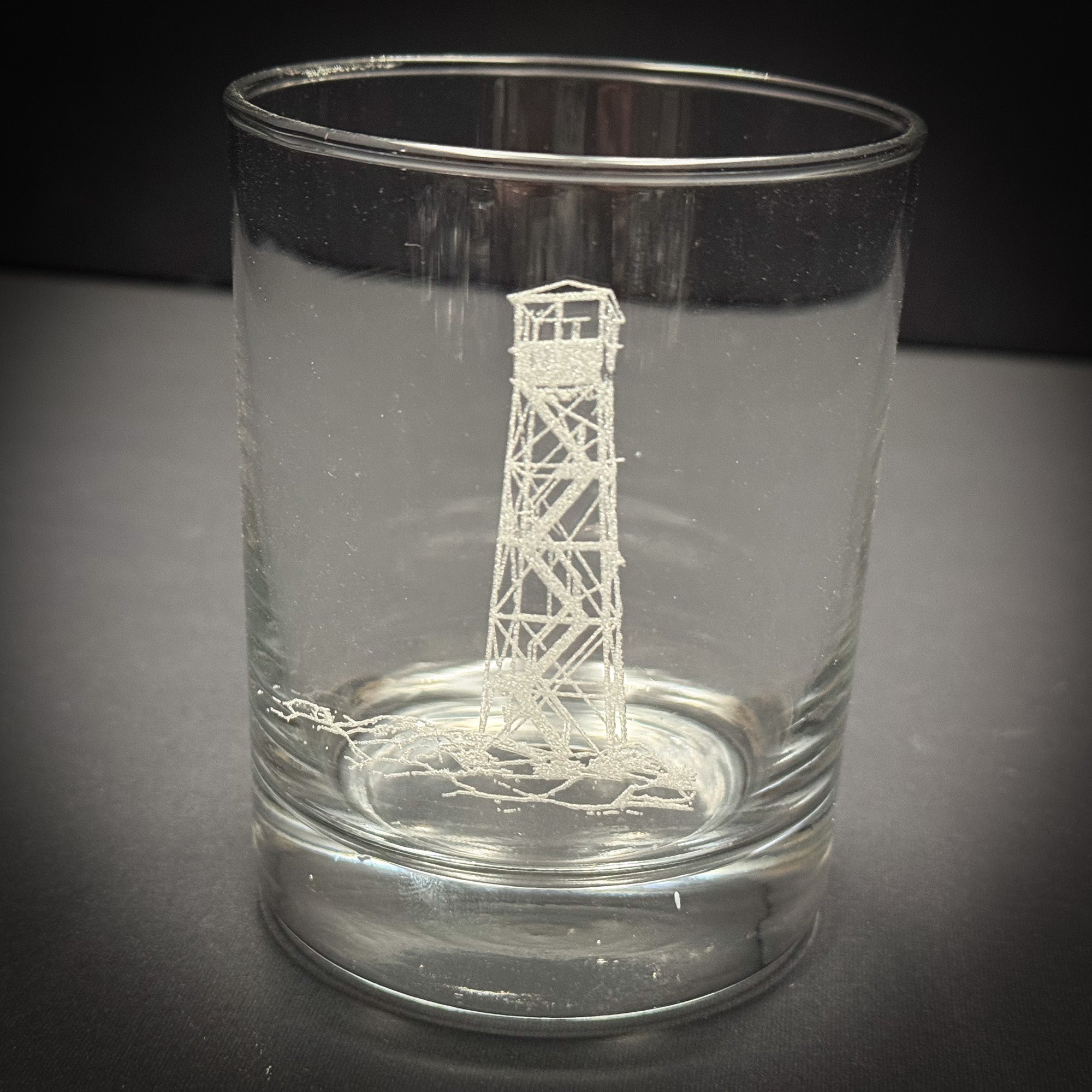 A clear glass with an etched image of a lighthouse on it.