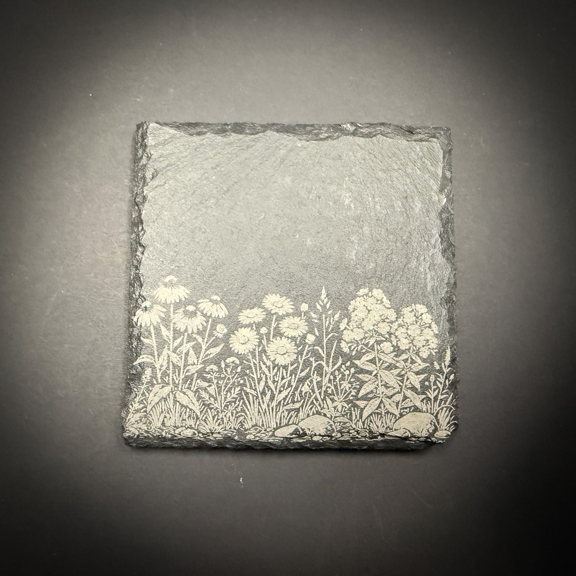 A square-shaped slate with a floral design on it, placed against a dark background.