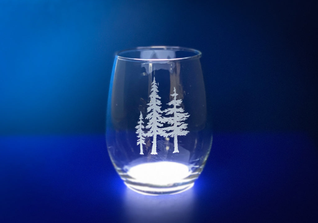 A clear glass with a white tree design etched onto it, set against a blue background.