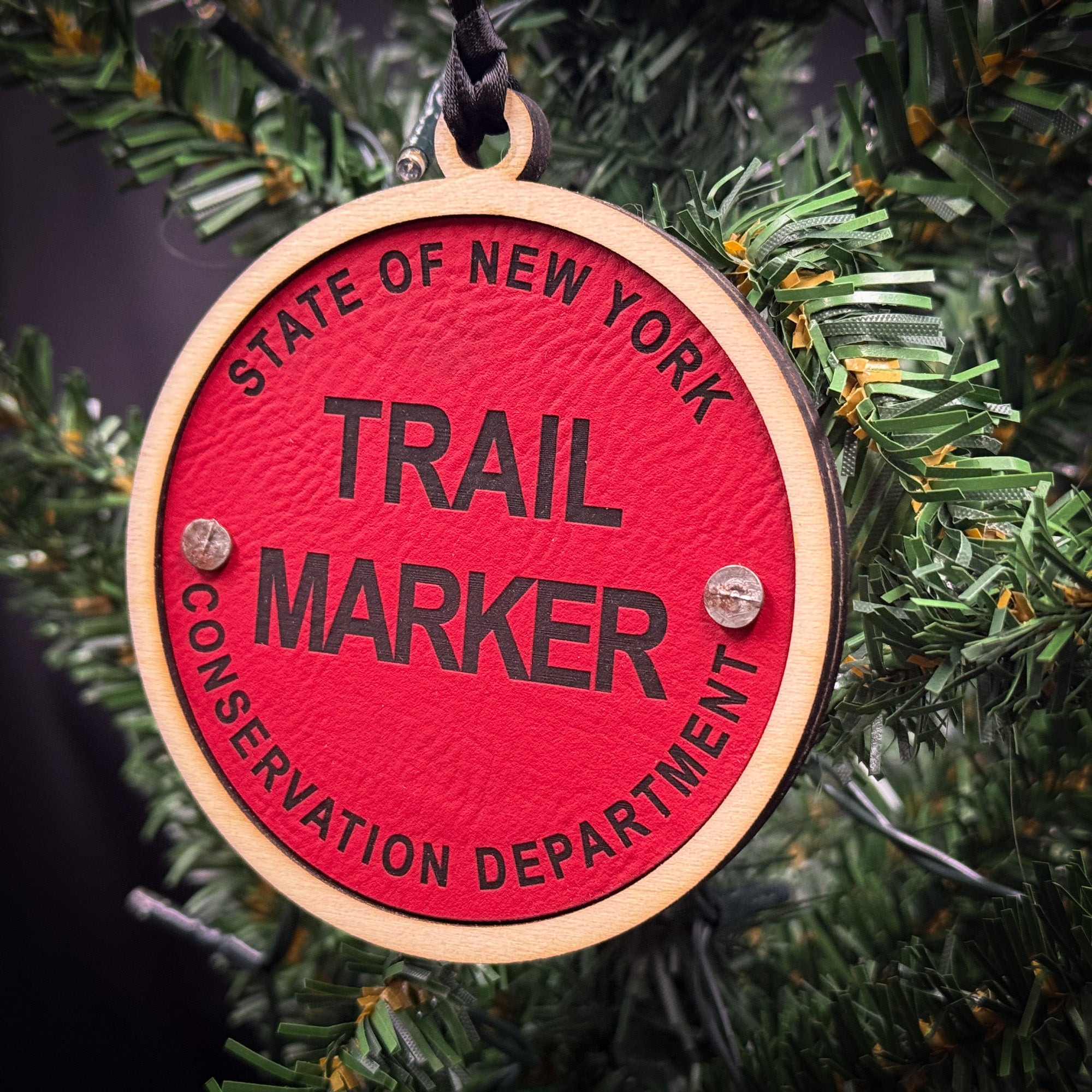 A red circular ornament with the text "TRAIL MARKER" printed on it, hanging on a Christmas tree.