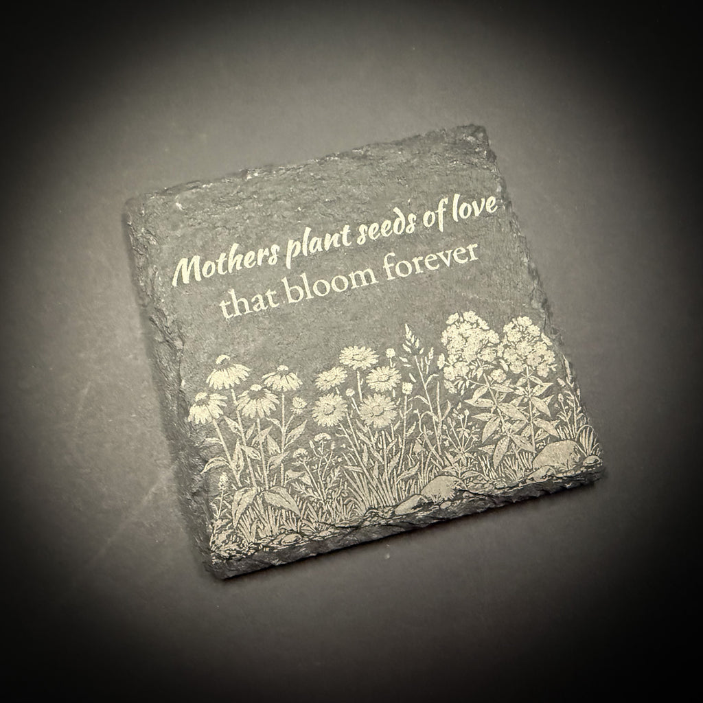 A square stone with a floral design and the text "Mothers plant seeds of love that bloom forever" engraved on it.