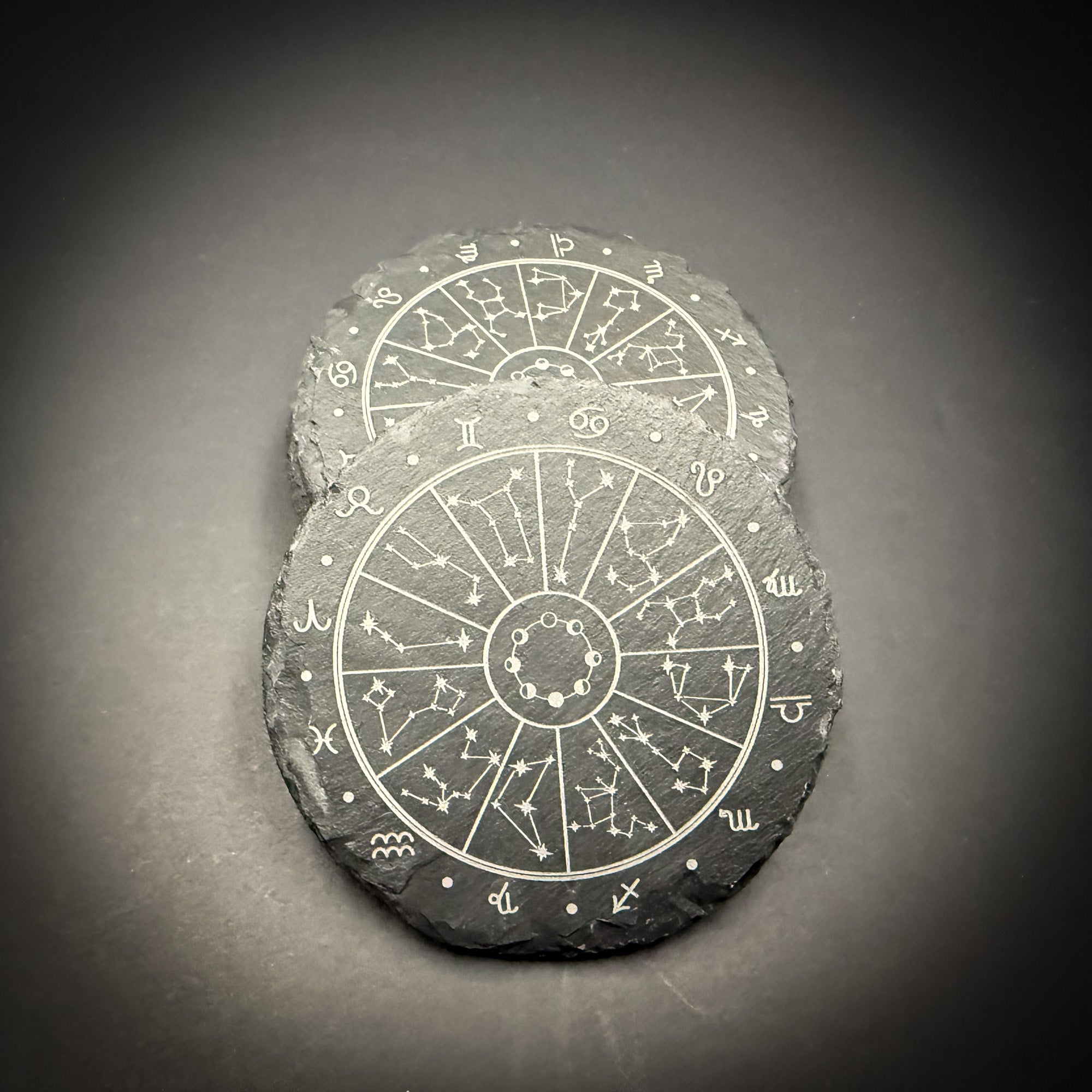 Two slate coasters with astrological charts and symbols printed on them.