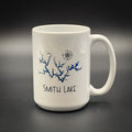 A white ceramic mug with a blue design depicting a river or lake, along with the text "SMITH LAKE" printed on it.