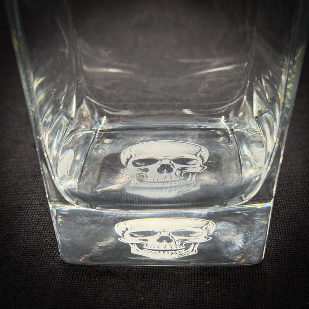 a clear glass with a skull design on it, placed on a dark surface.