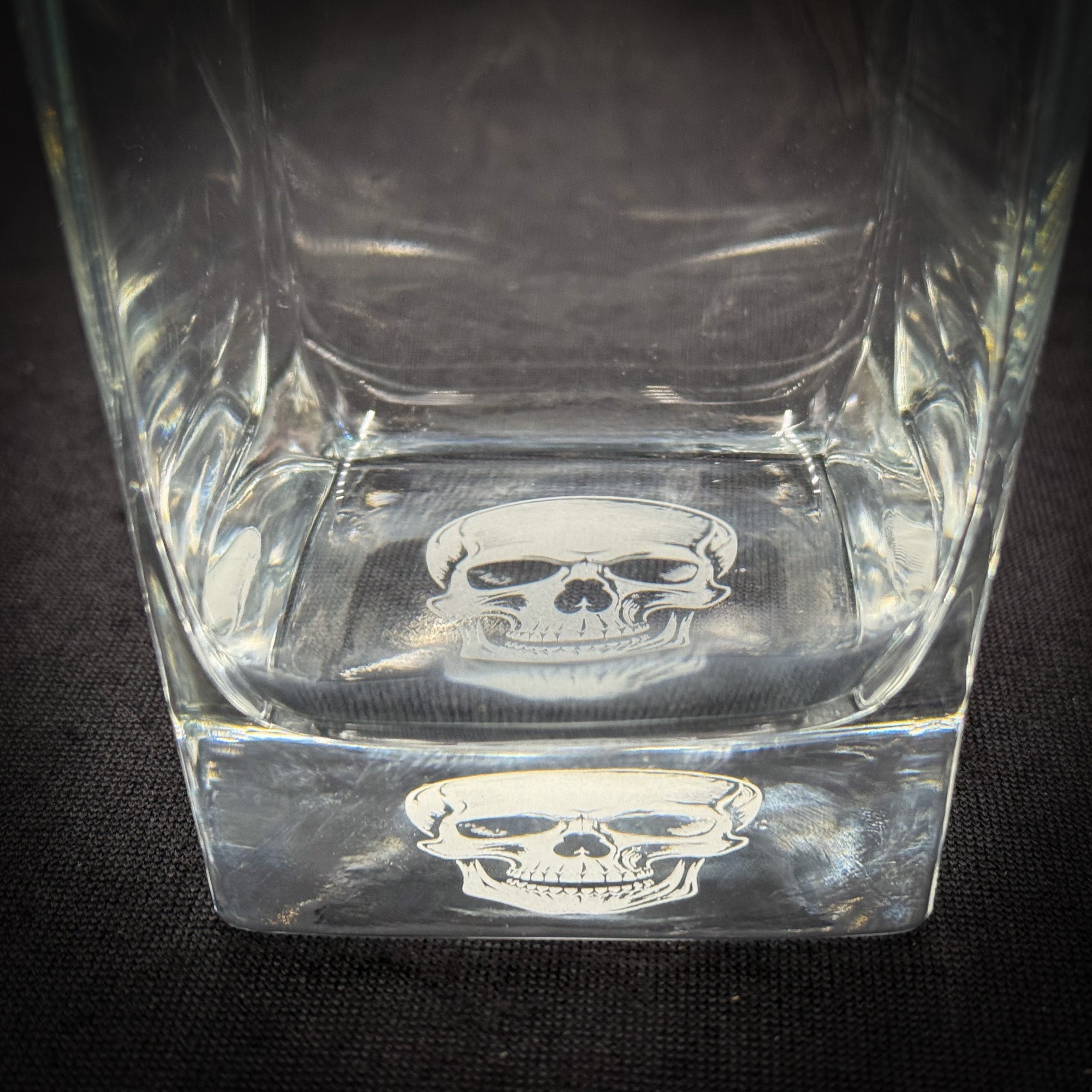 a clear glass with a skull design on it, placed on a dark surface.