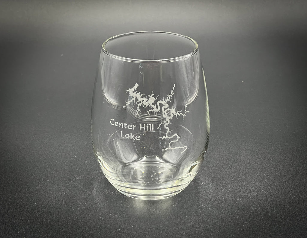 A clear glass with a design etched onto it, sitting on a dark surface.
