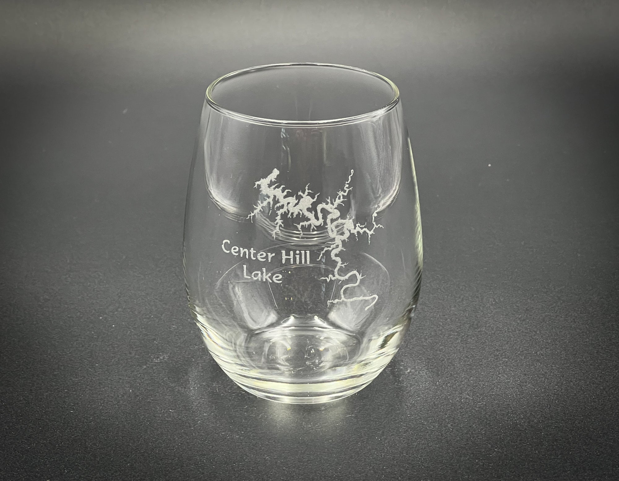 A clear glass with a design etched onto it, sitting on a dark surface.